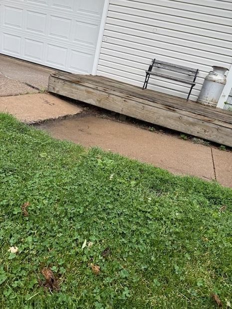 Tilted wooden ramp beside a garage, with cracked concrete and grass in the foreground.