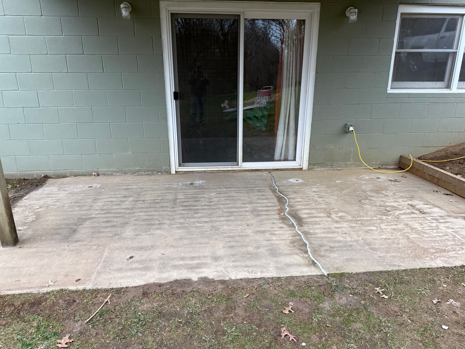 Concrete patio with a sliding glass door, brick wall, and small window beside a grass lawn.