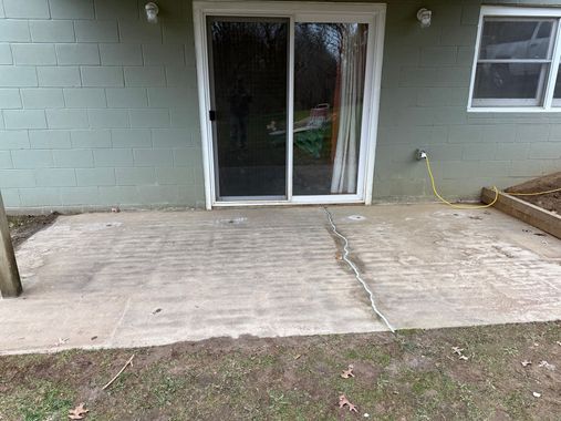 Concrete patio with a sliding glass door, brick wall, and small window beside a grass lawn.