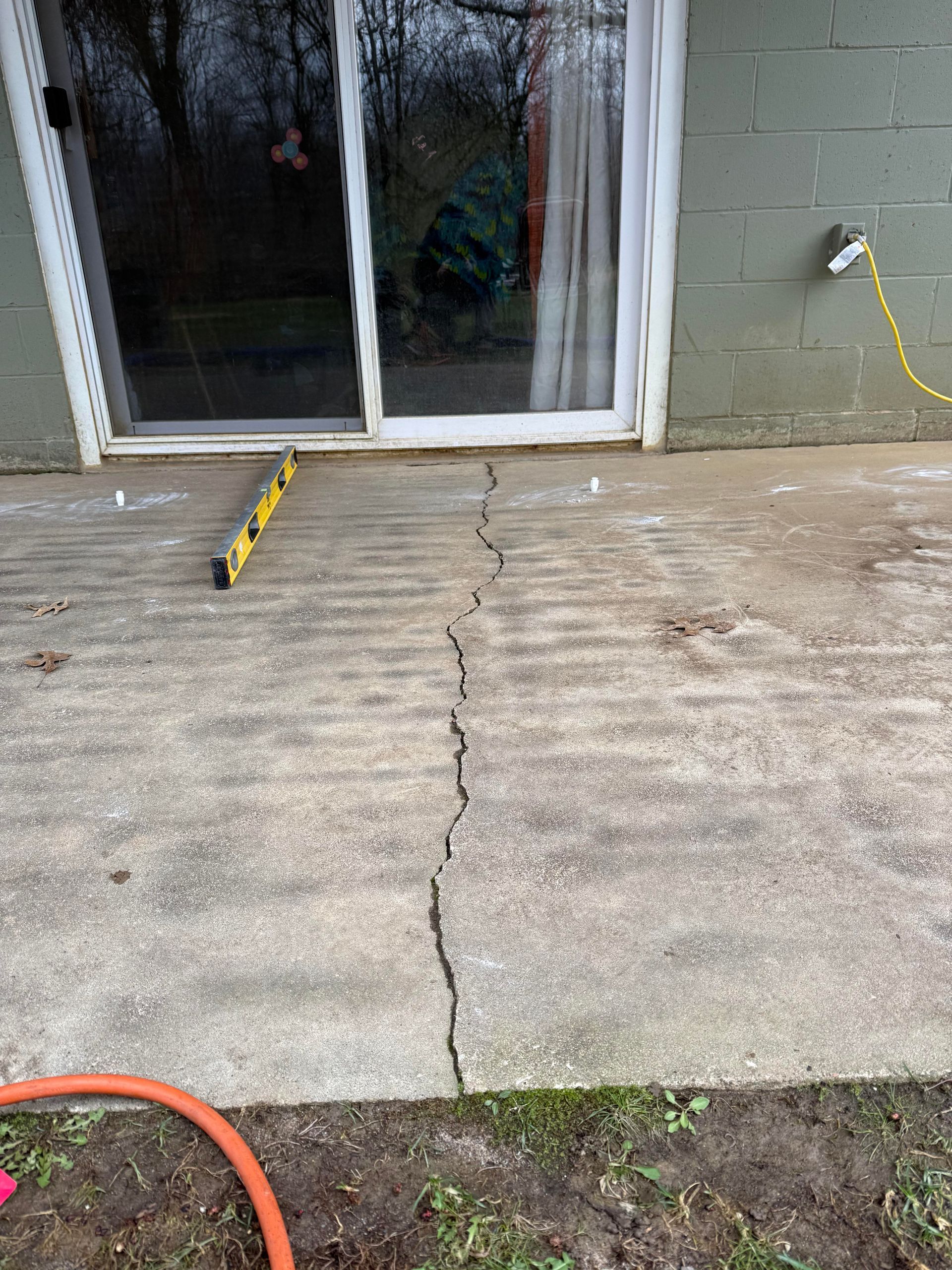 Cracked concrete patio in front of sliding glass door, with a yellow cable on the left and hose at bottom.