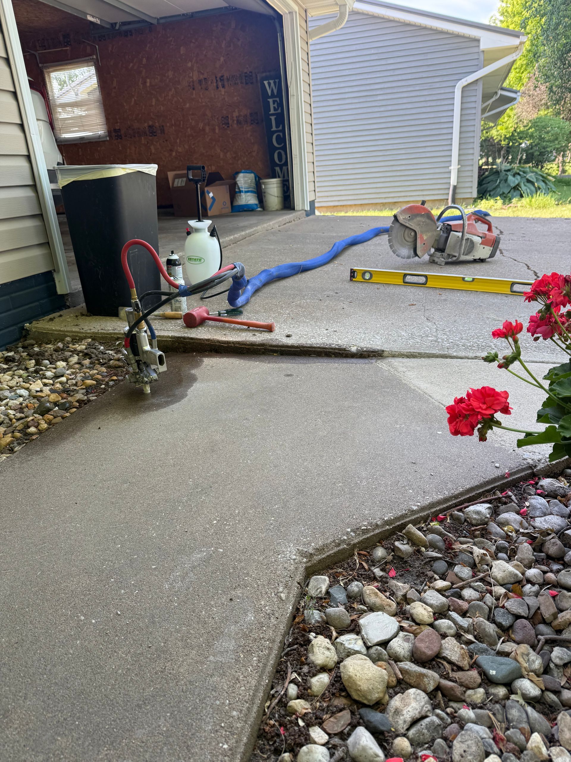 Concrete patio under construction with power tools, hoses, and stones beside a garage garden area