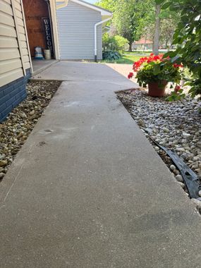 Concrete walkway between houses beside white rocks and red flowers in a planter.