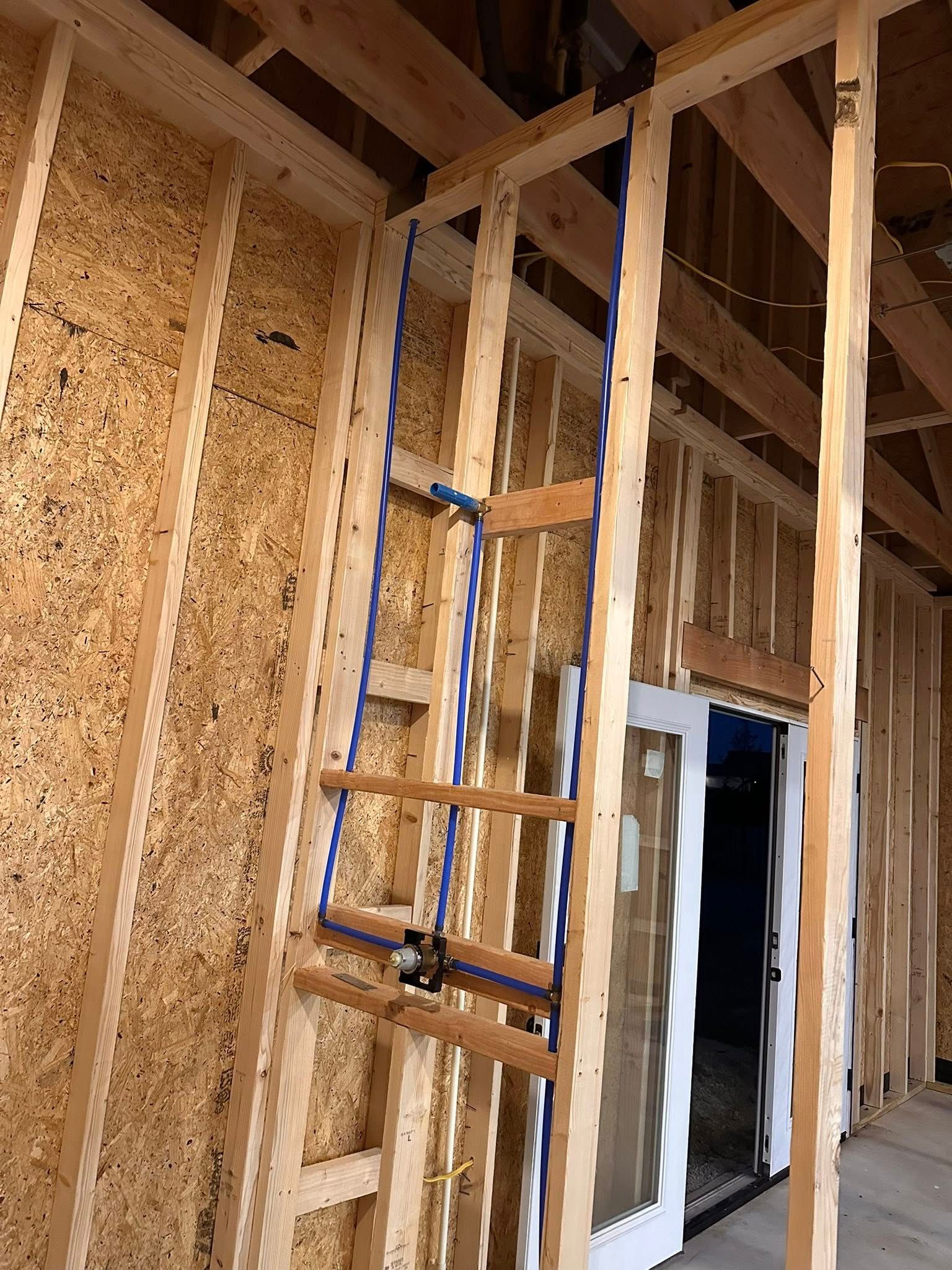 A blue shower valve assembly mounted between wooden wall studs at a construction site.