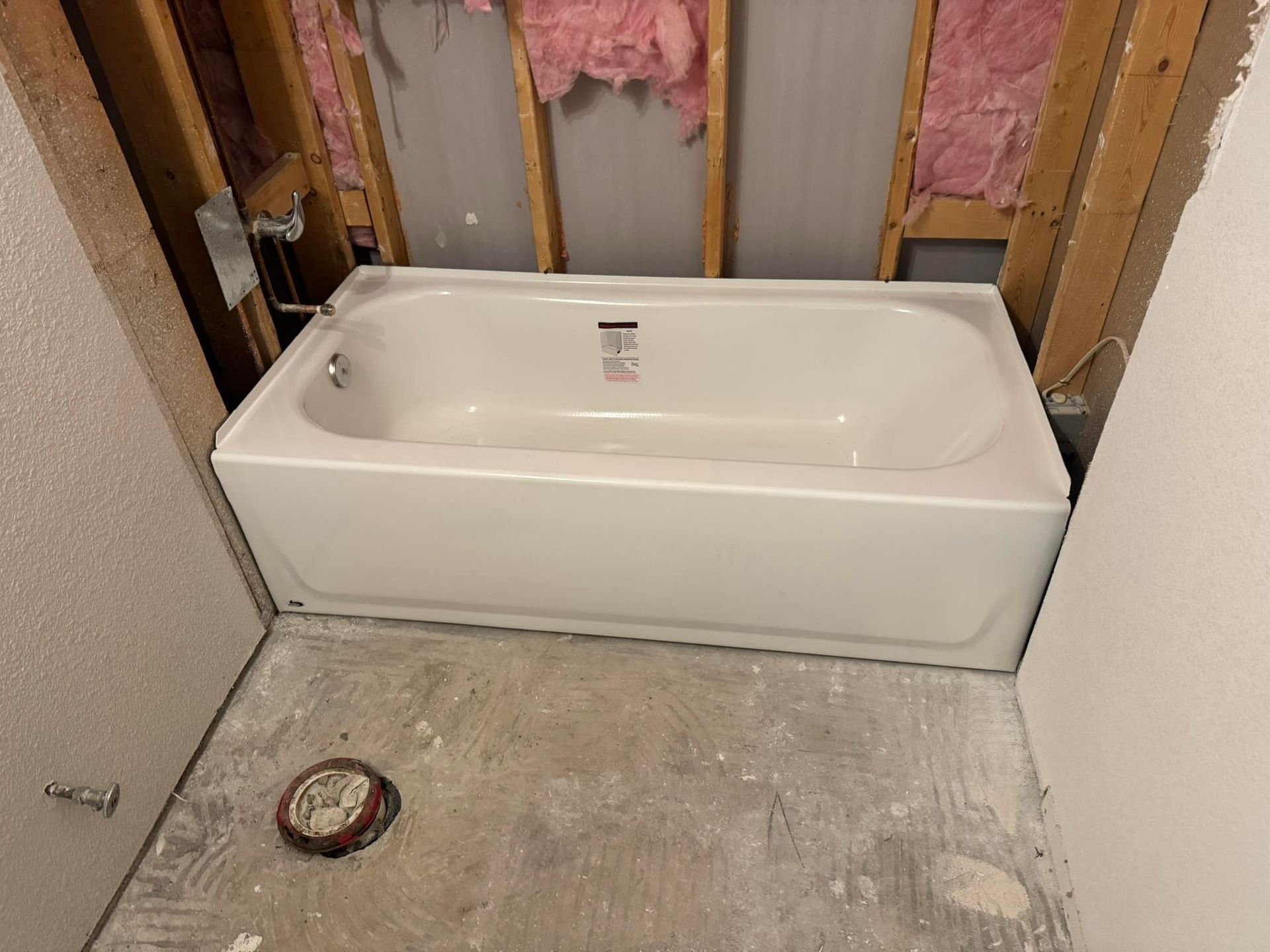 A white bathtub installed in a bathroom alcove with exposed wall studs and pink fiberglass insulation.