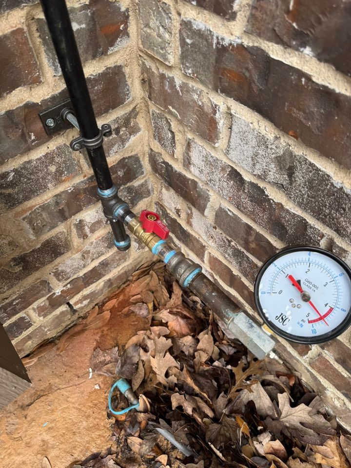 A black gas pipe attached to a brick wall with a brass valve and a pressure gauge showing a reading of 25 psi.