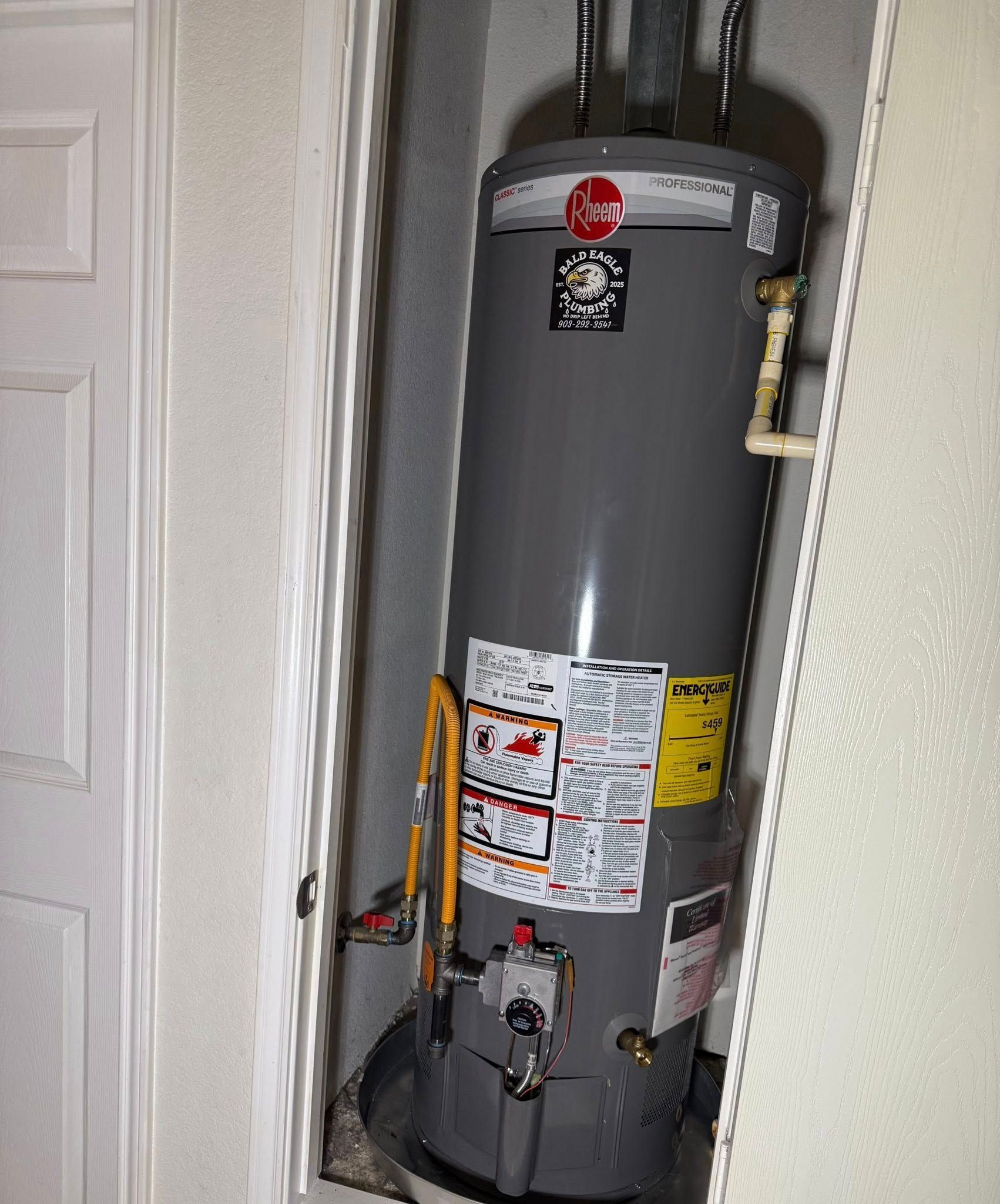 A gray Rheem water heater sits inside a closet, connected to pipes and installed in a drainage pan.
