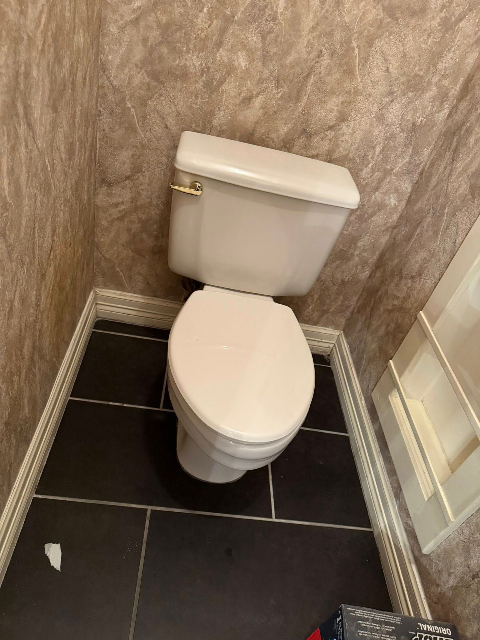 A white toilet with the lid closed in a small room with textured tan walls and dark tile floors.