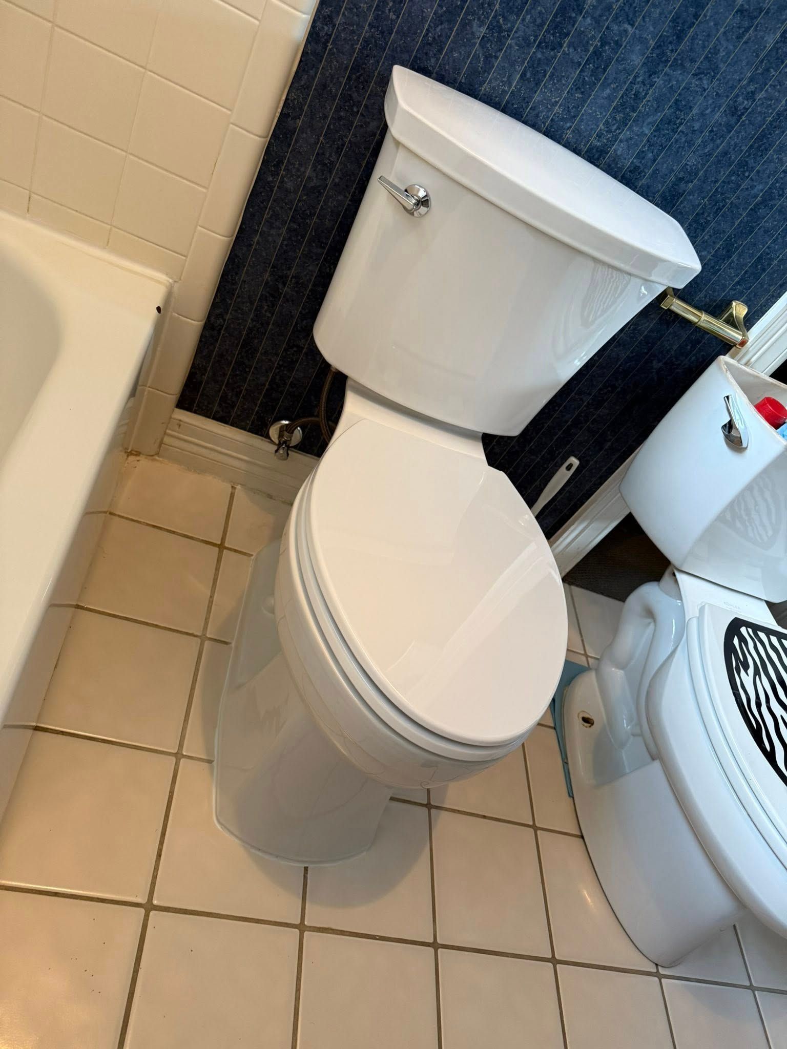 A white toilet in a bathroom with beige tiled floors and dark blue wallpaper.