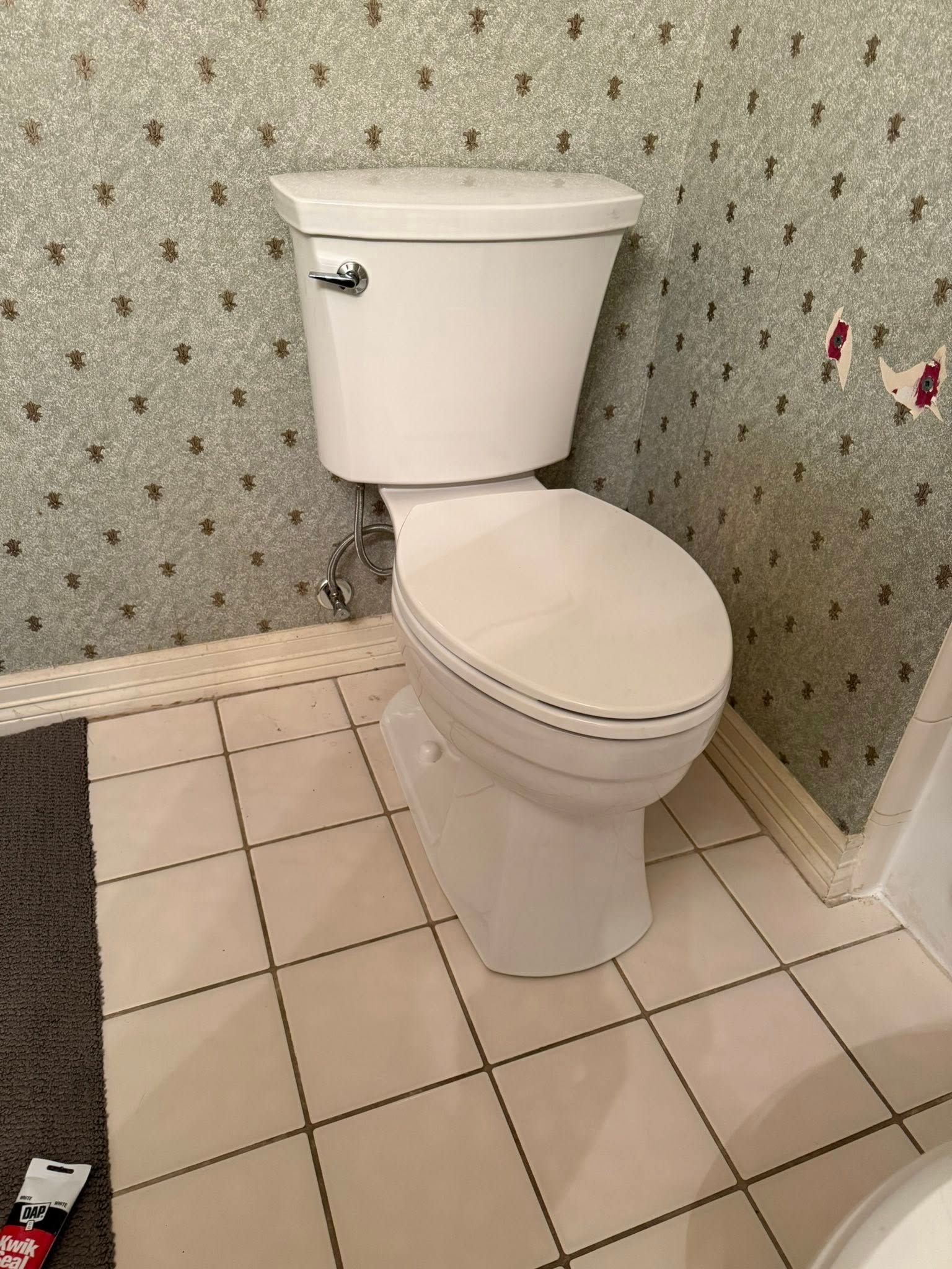 A white toilet in a bathroom with patterned green wallpaper and white tiled flooring.