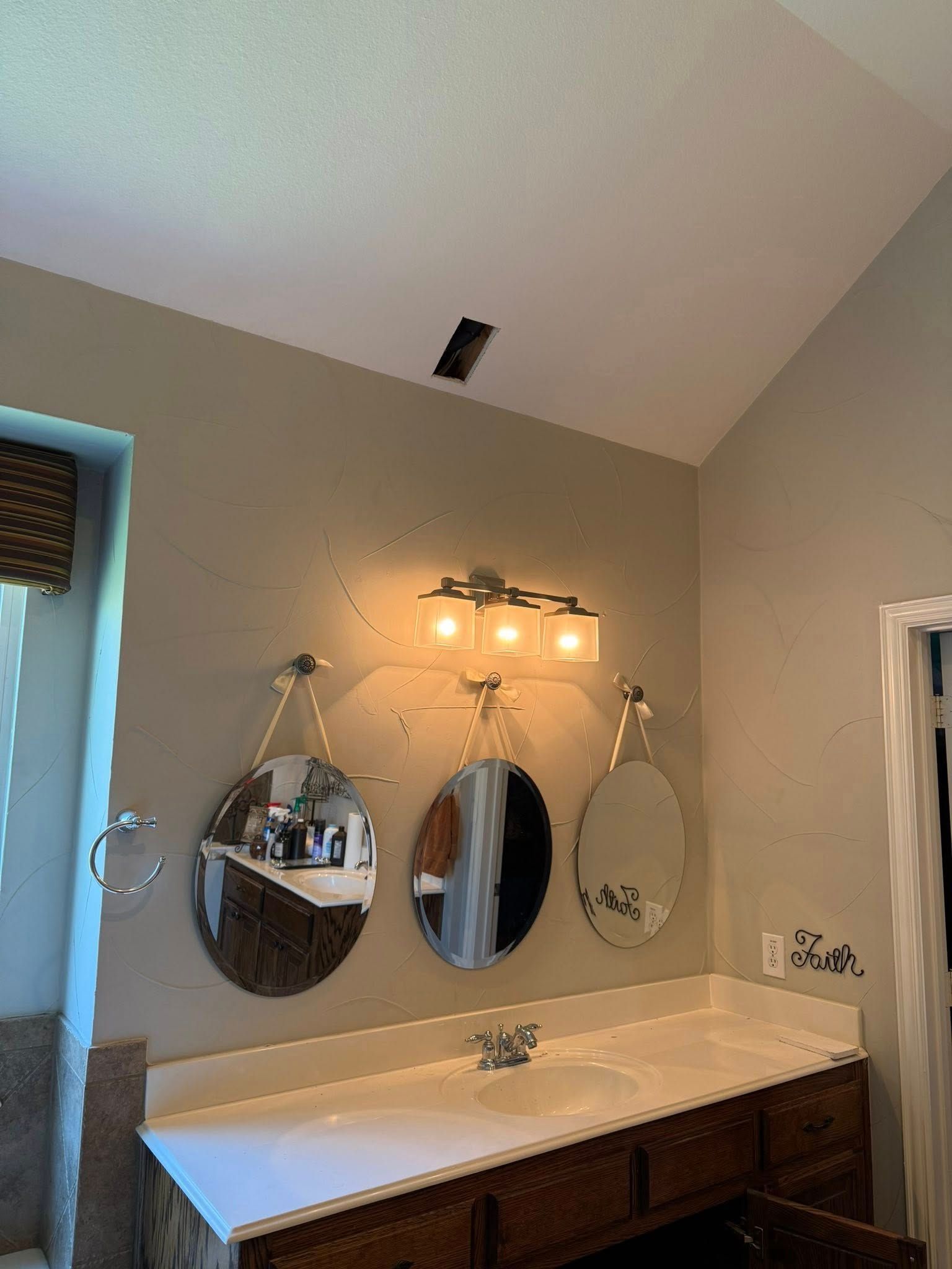 Bathroom vanity with a white countertop, two sinks, and three oval mirrors hanging below a single light fixture.