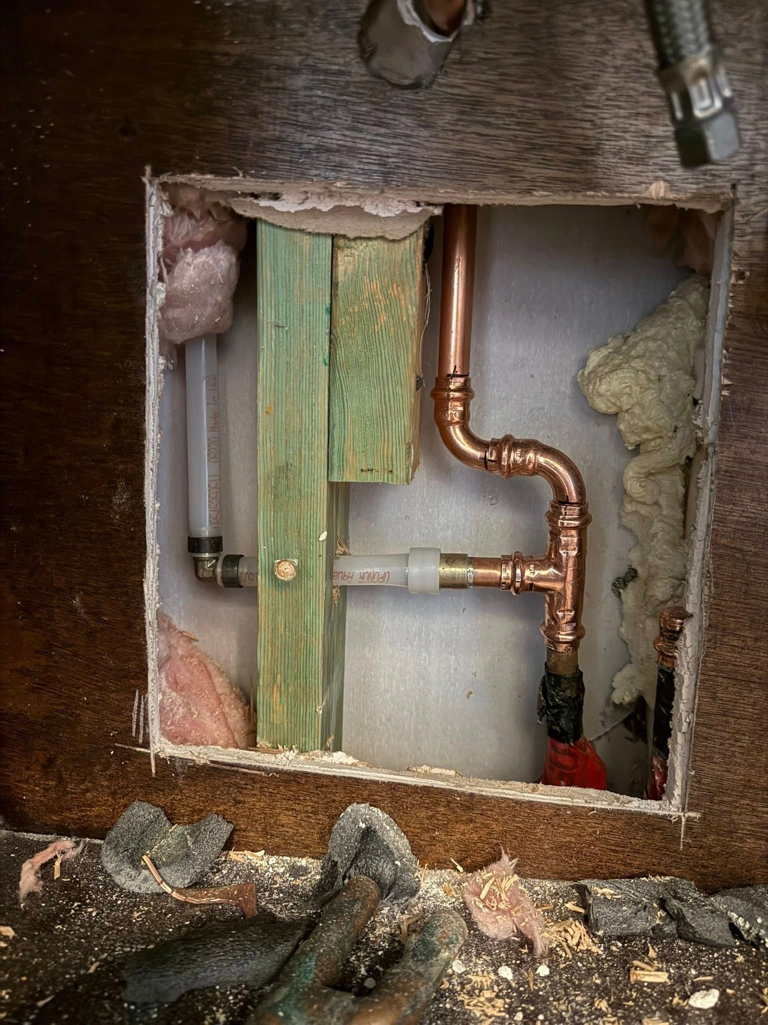 A wall cavity showing copper and PEX plumbing pipes connected with couplings and elbows, installed near a wooden stud.