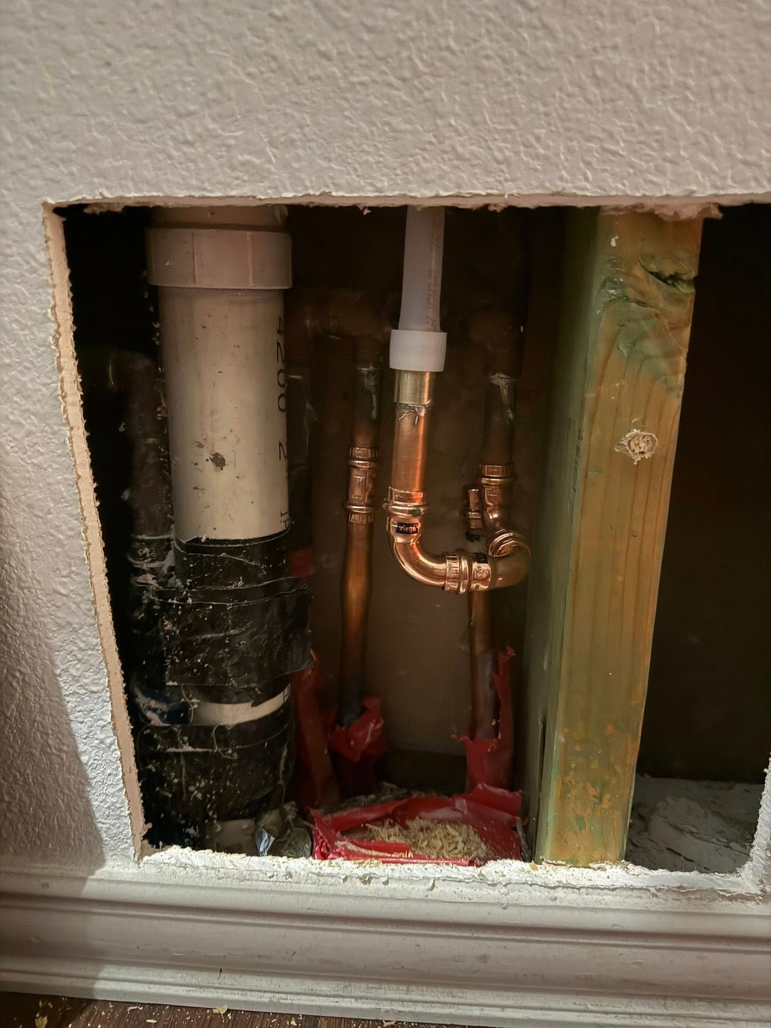 An exposed wall cavity showing PVC plumbing and copper pipes connected to a white fixture supply line.