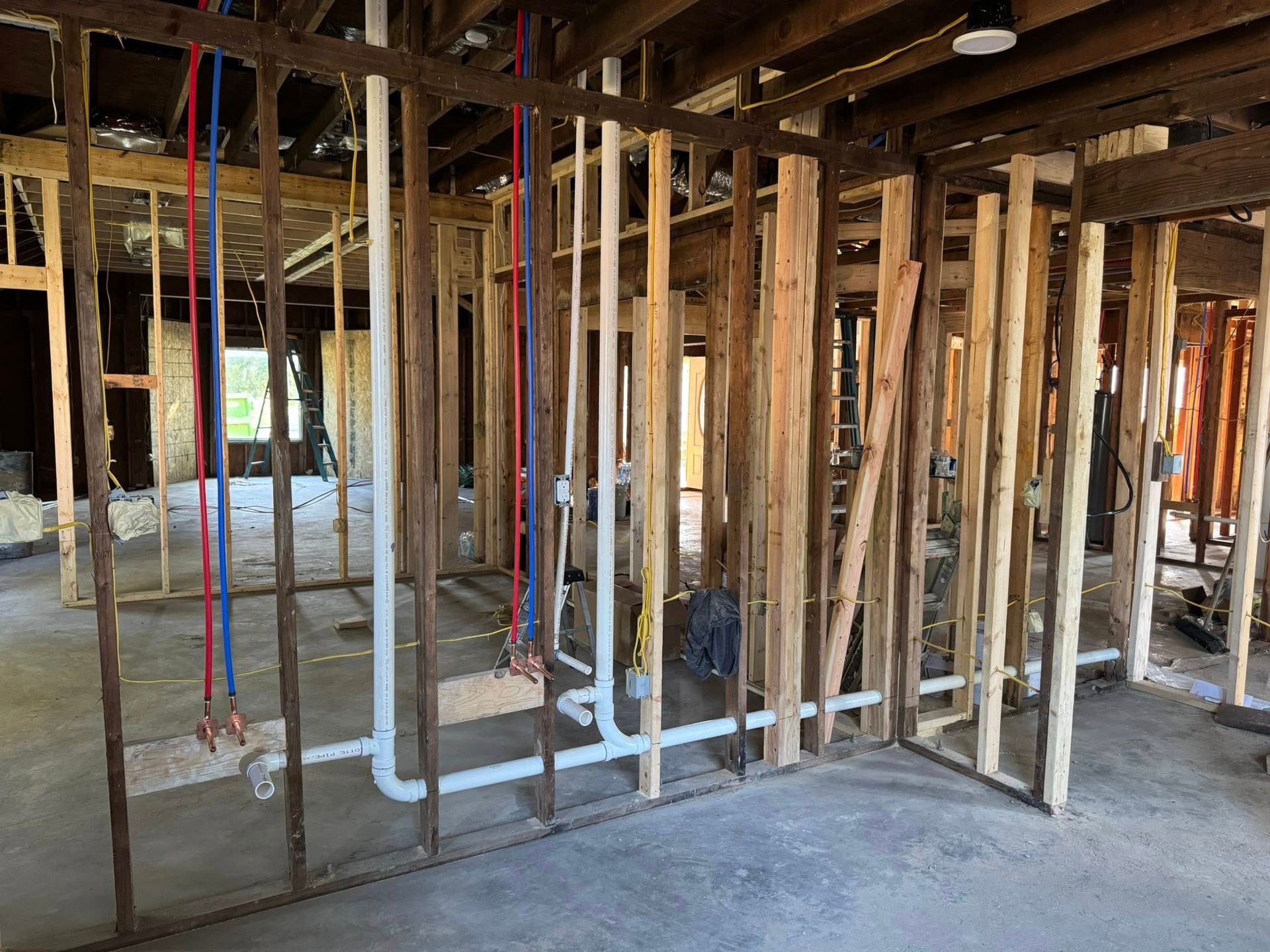 Framed interior of a house under construction, featuring exposed wooden studs and newly installed white PVC plumbing pipes.