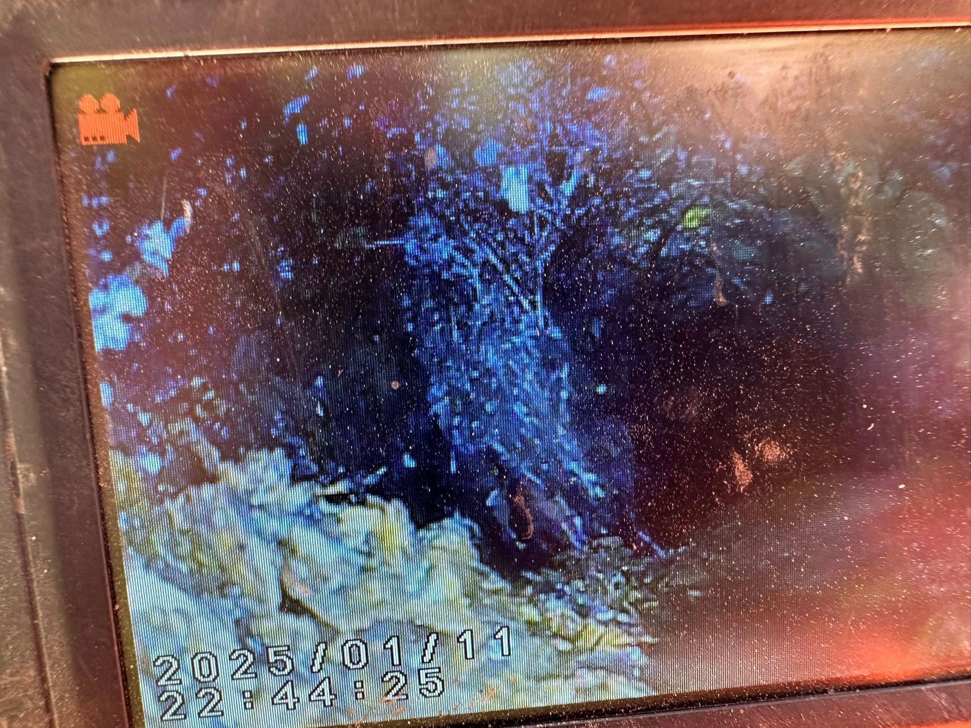 A low-quality, dark digital screen capture showing a textured, blue-toned interior, likely from a pipe inspection camera.