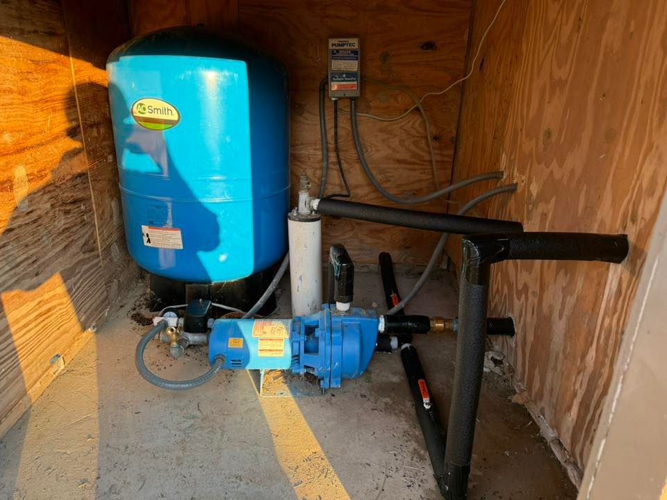 A blue well pressure tank and pump system sit on a concrete floor in a wooden enclosure.