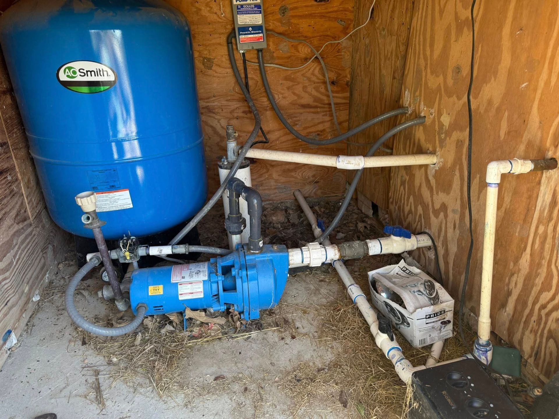 A residential well water system featuring a blue storage tank, a blue water pump, and piping inside a wooden enclosure.