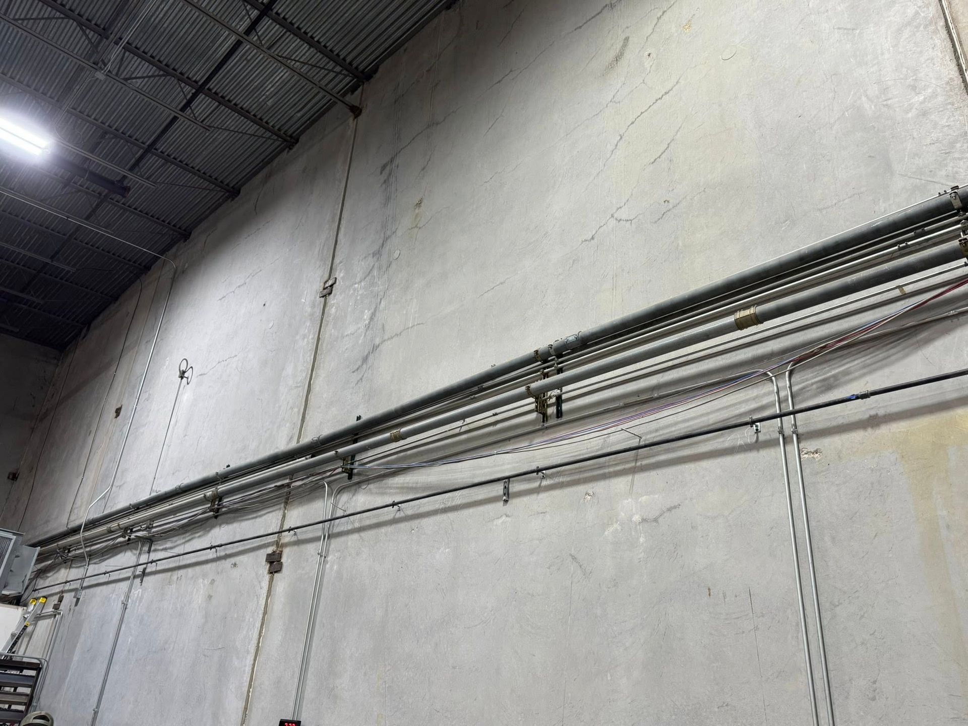 Metal conduit pipes run horizontally across a textured, light-colored industrial wall below a dark, ribbed ceiling.