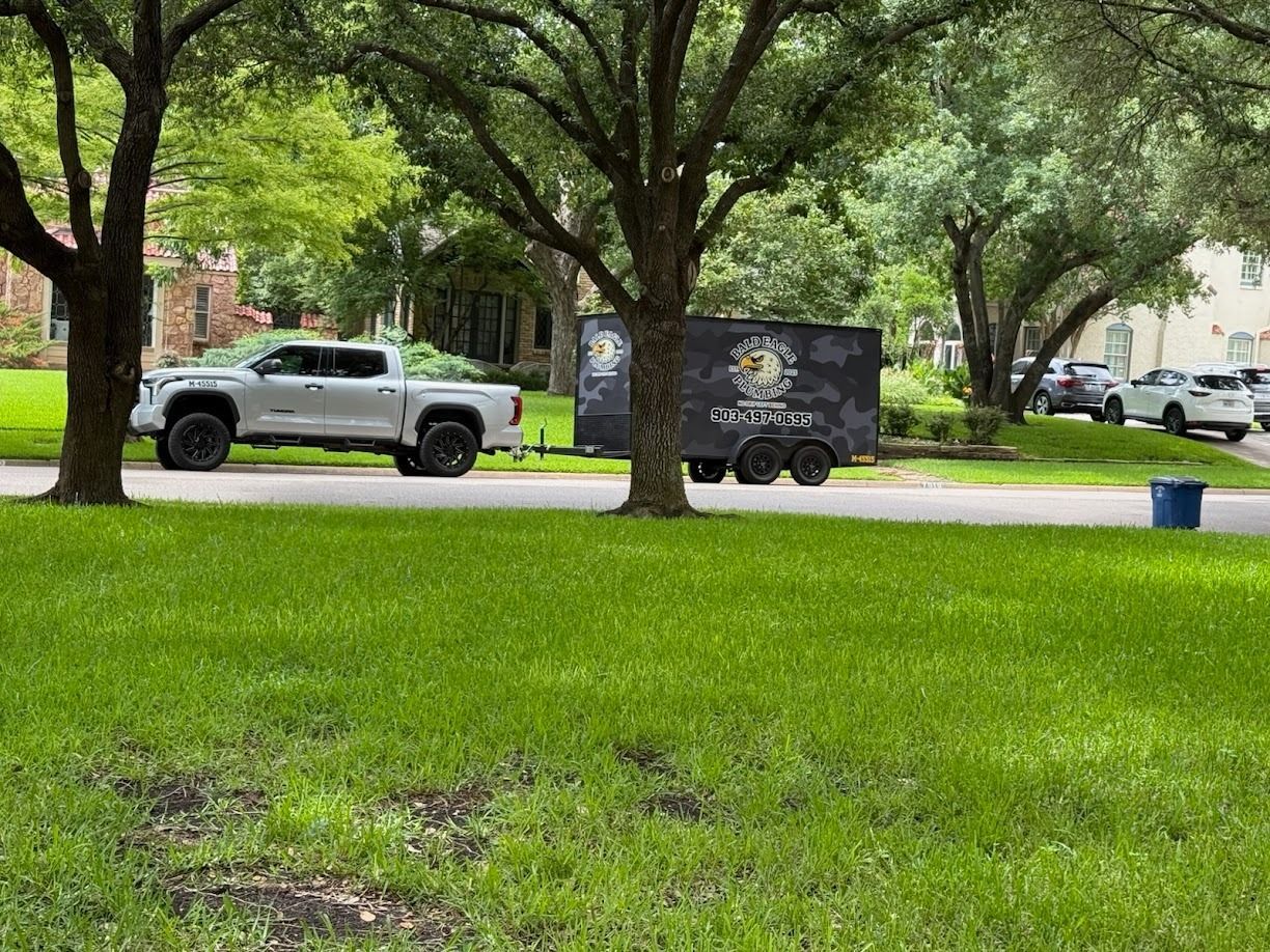 A white pickup truck towing a dark, logo-covered utility trailer parked on a suburban residential street.