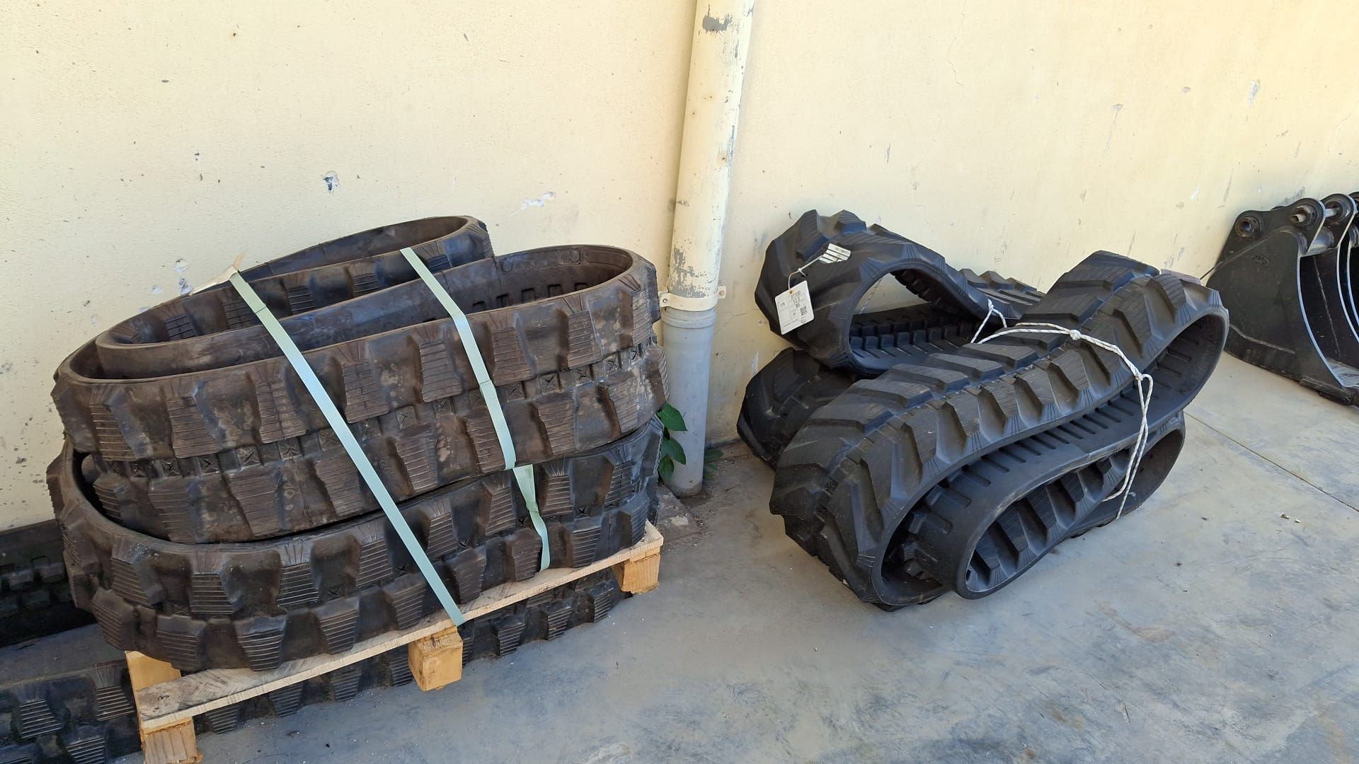 Pneumatici neri impilati e fissati su pallet di legno contro un muro su un pavimento di cemento.