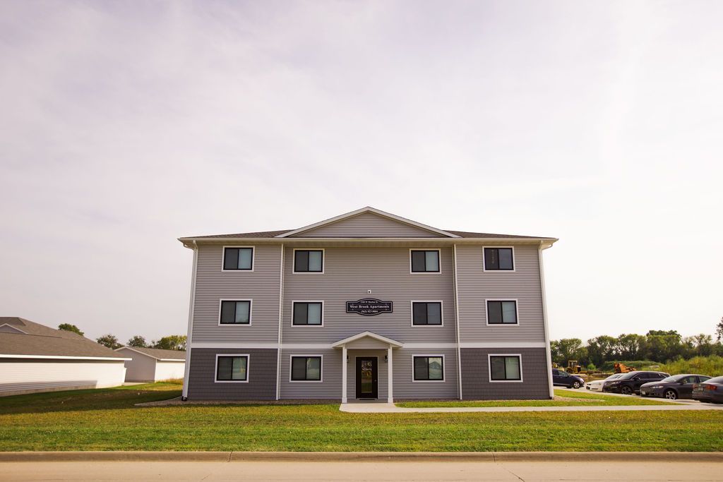 A large apartment building with a lot of windows is sitting on top of a lush green field.