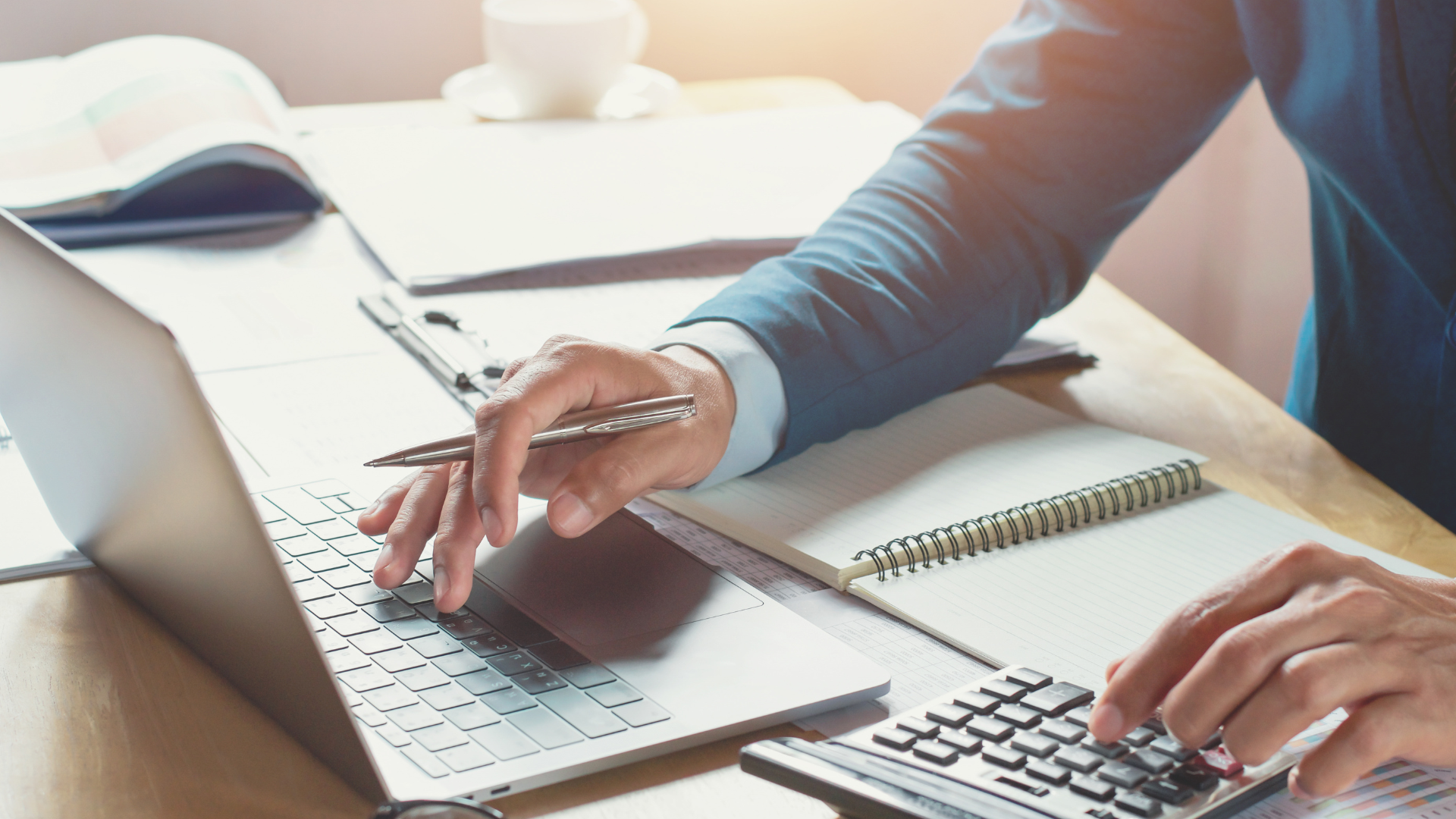 Person typing on a laptop at a desk with a notebook and calculator nearby