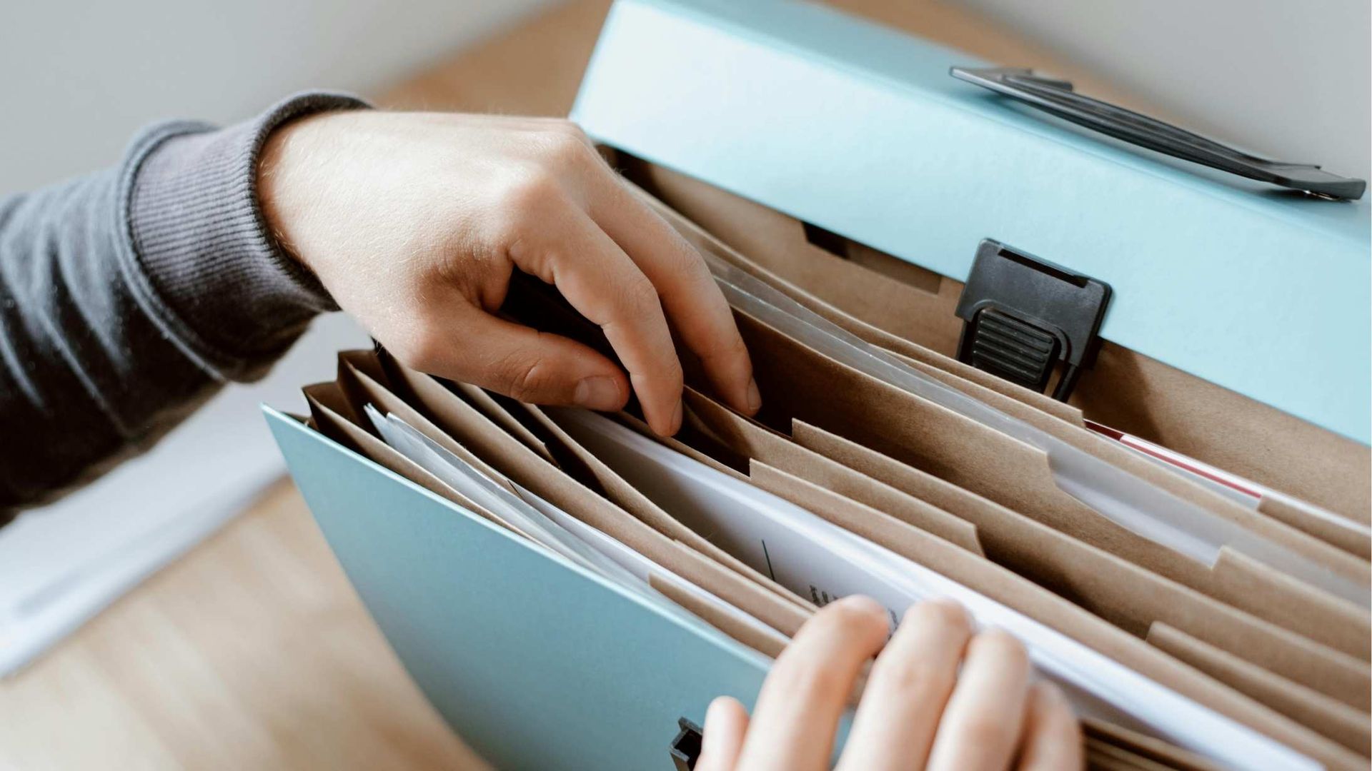 Hands sorting papers in a light blue file organizer with folders and documents visible