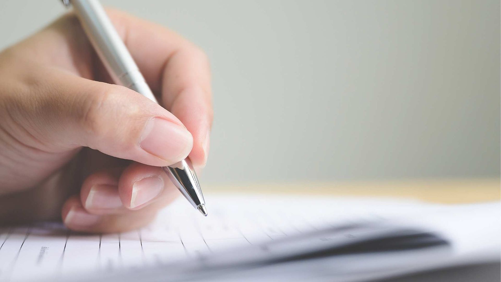 Hand holding a pen over paper, writing on a notebook in close-up.