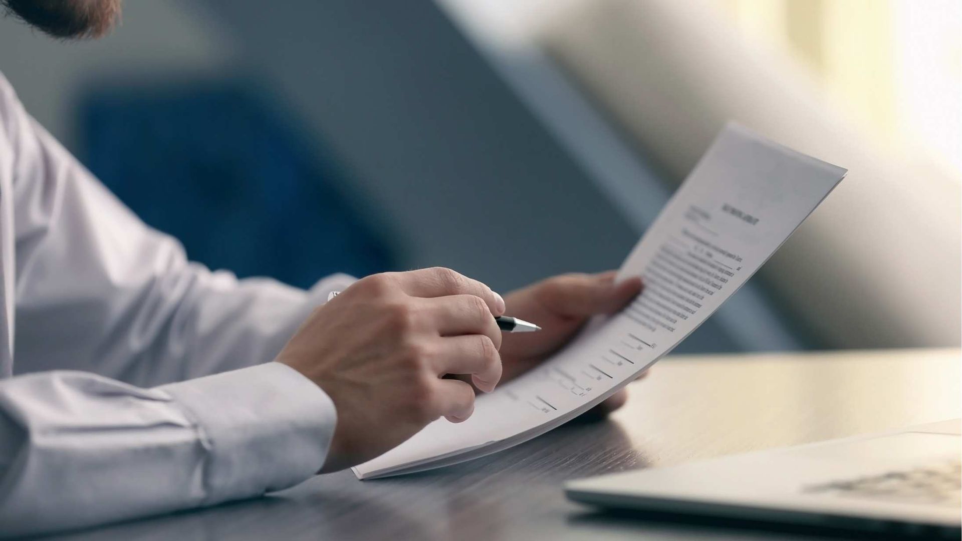 Hand holding a pen over a document at a desk in a bright office setting