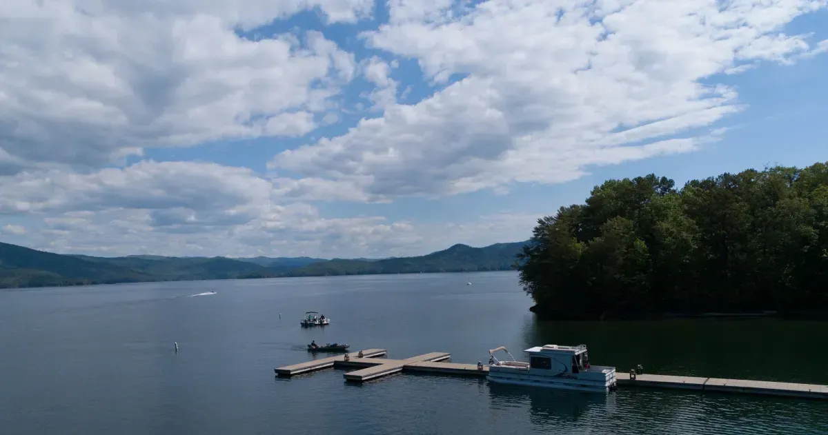 Lakeside dock with a small boat under a cloudy sky, calm water and forested shore in the background