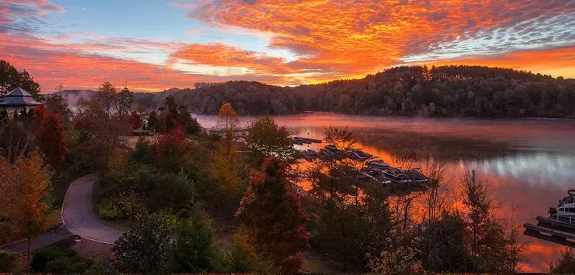 Sunset over a misty lake with autumn trees and hills reflected in the water