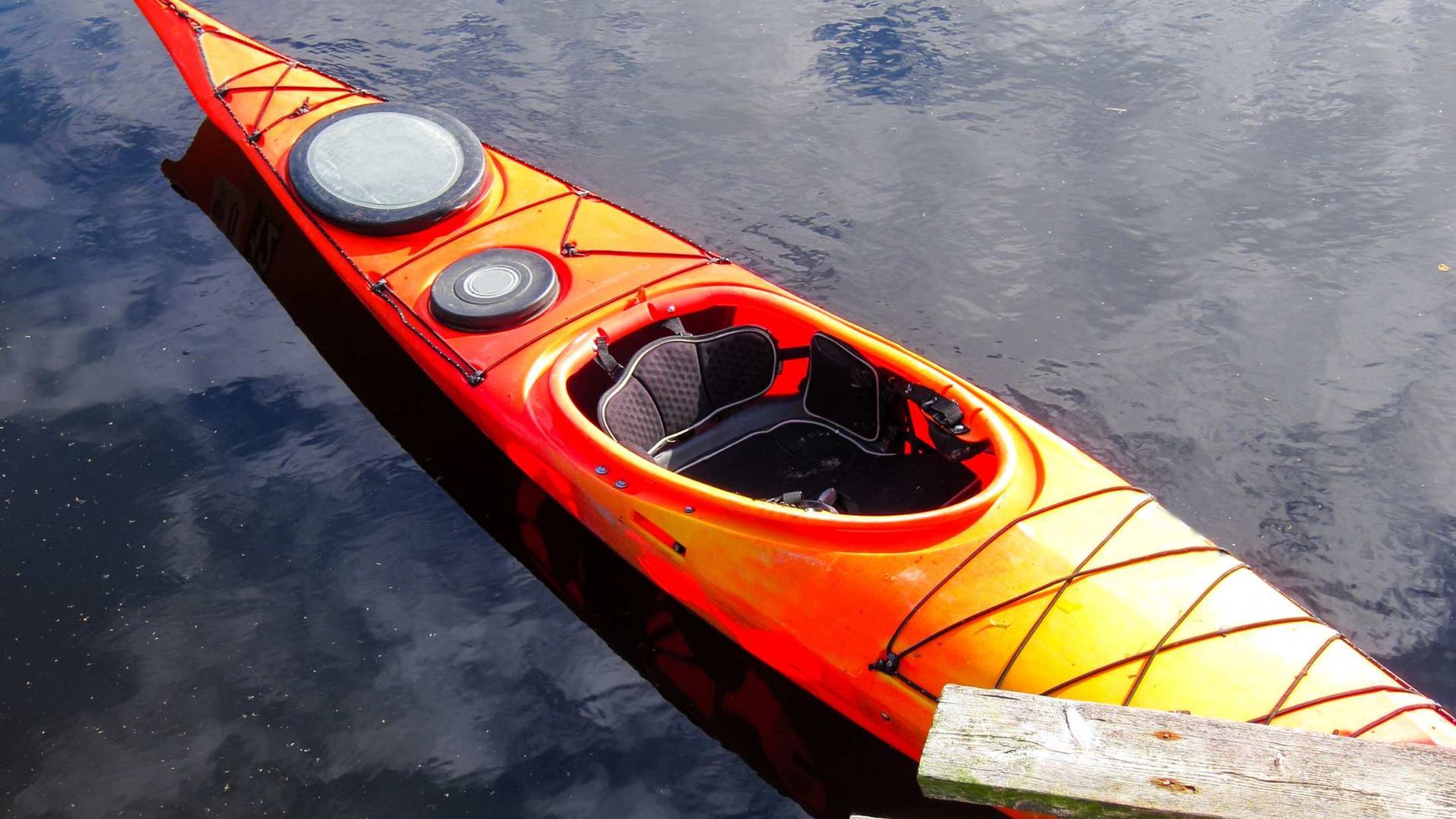 Red kayak floating on dark water, viewed from above, with two hatches and cockpit visible