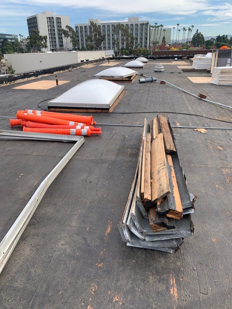 Rooftop construction area with stacked materials, orange pipes, and white skylights in progress