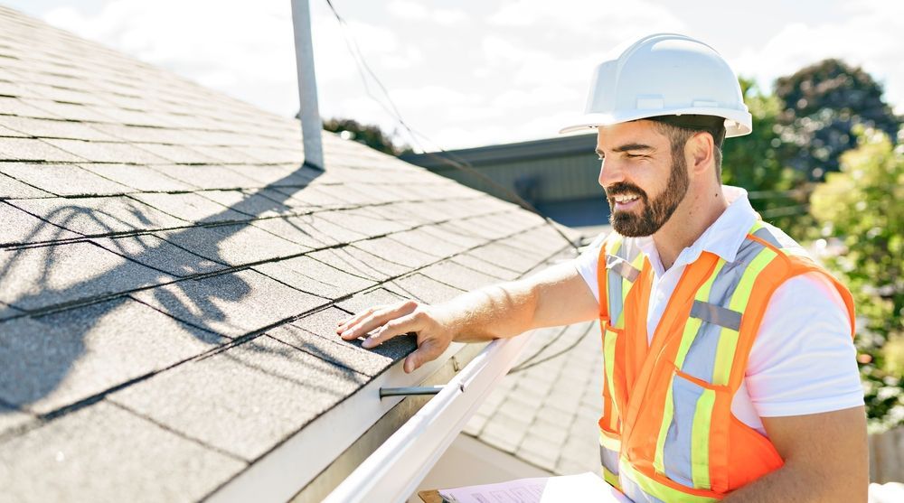 Worker in hard hat inspecting roof shingles with a clipboard on a sunny day