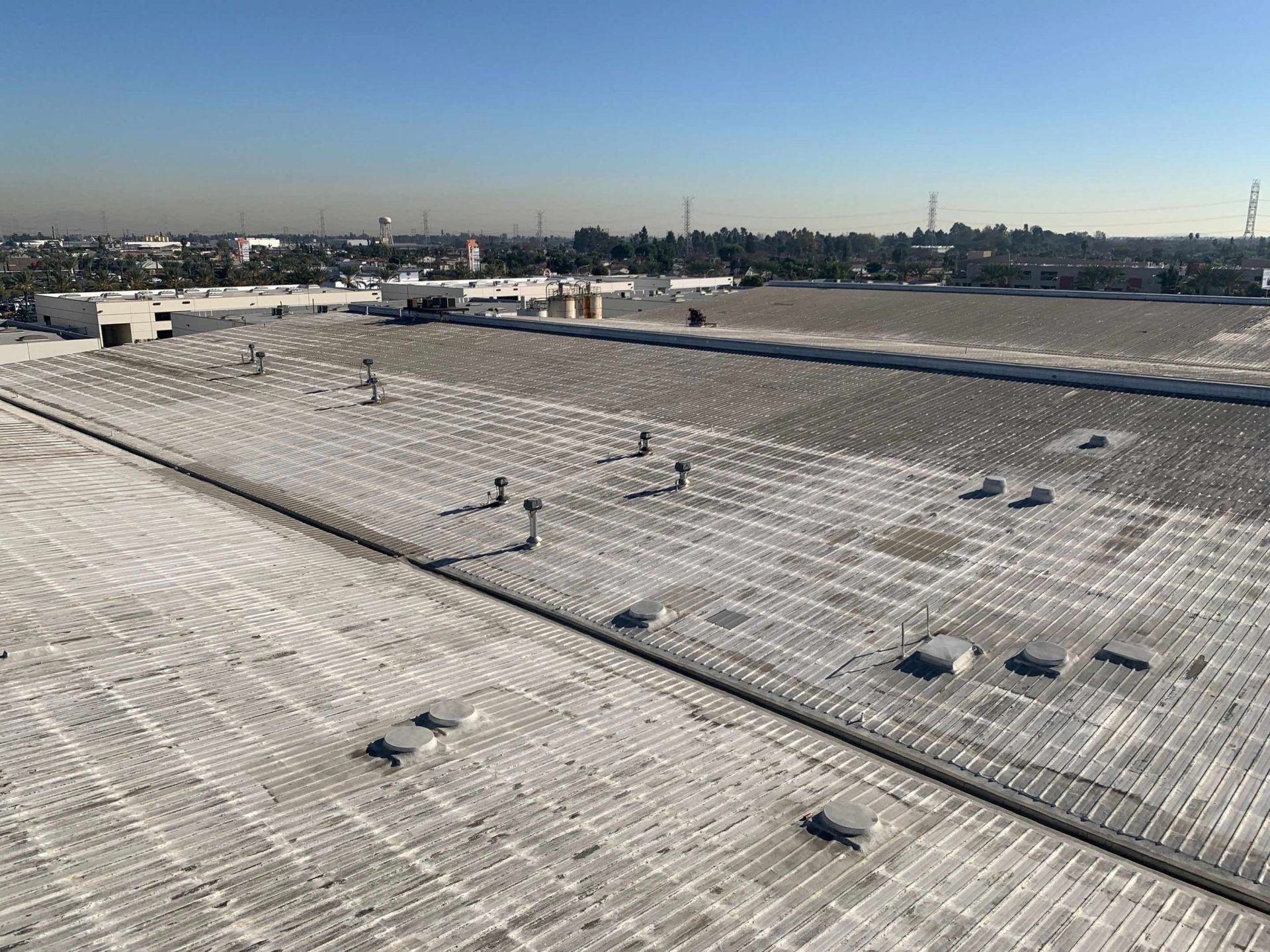 Snow-covered rooftop with scattered vents under a clear blue sky, city skyline in the distance