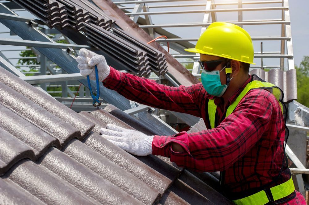 Worker in yellow hard hat securing roof tiles with a tool on a sloped roof