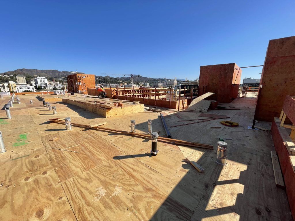 Construction site with wooden rooftop framing, brick walls, and city buildings under a clear blue sky