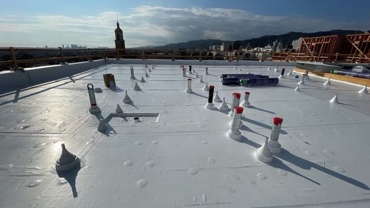 White rooftop with vents and red caps under a cloudy sky, with a distant tower and bridge.