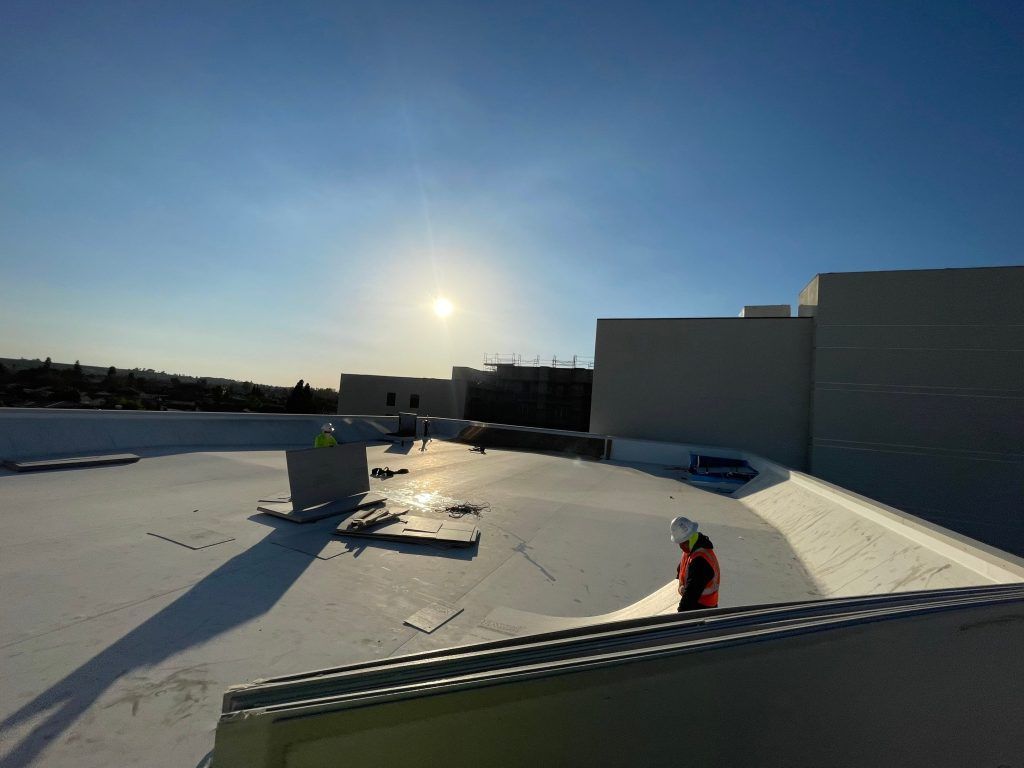 Roofer in red jacket working on a flat white rooftop at sunset.