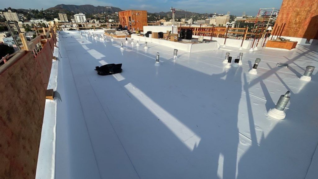Rooftop covered in white coating with vents and shadows, overlooking a cityscape in the distance