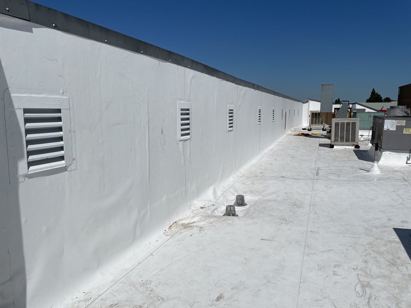 White rooftop walkway beside a long white wall with vents under a clear blue sky