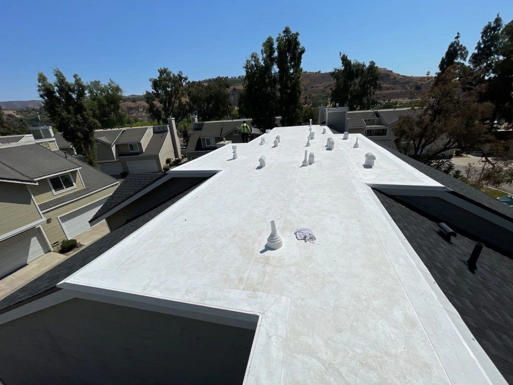 White rooftop with vents overlooking suburban houses and trees under a clear sky