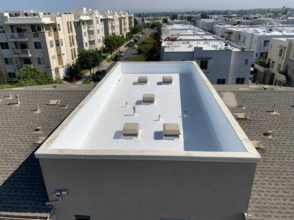 Rooftop with a white flat roof and skylights in a residential apartment complex under a clear sky