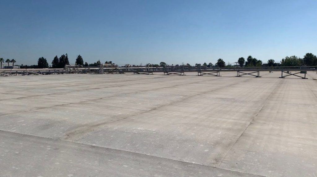 Empty paved lot under a clear sky with a line of trees in the distance