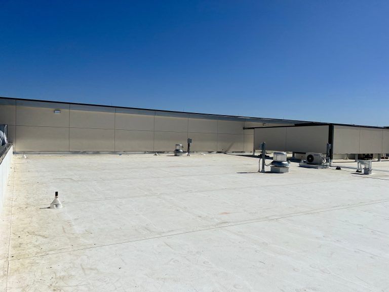 Rooftop with bright white surface, low beige building, and clear blue sky.