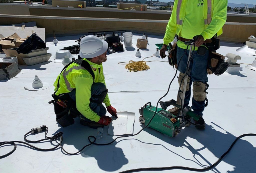 Two workers in neon jackets kneel on snow beside equipment and cables outdoors