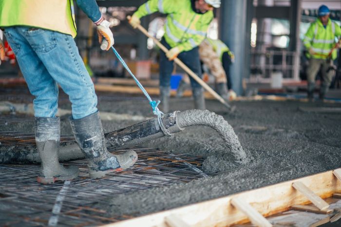 Construction workers pouring concrete onto a surface, wearing safety vests and boots.