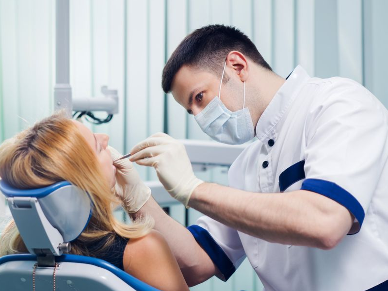Woman smiling, pointing to a dental model showing a tooth implant, blue background.