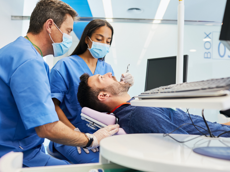 Woman smiling, pointing to a dental model showing a tooth implant, blue background.