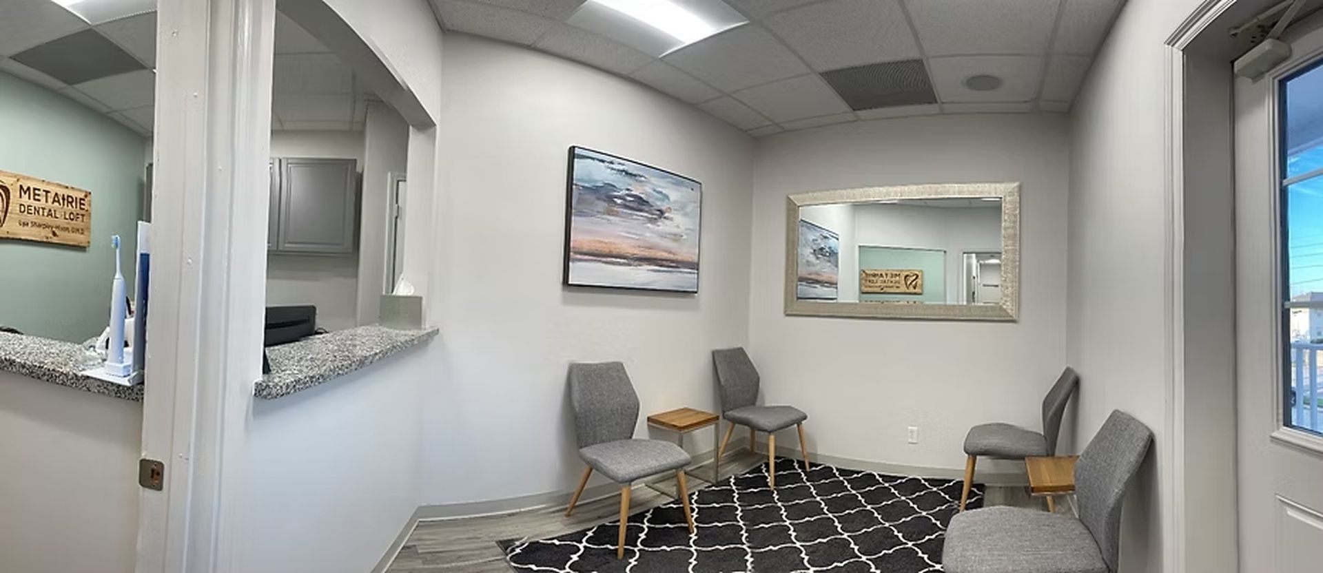 Waiting area with gray chairs, a black and white patterned rug, and a framed mirror.