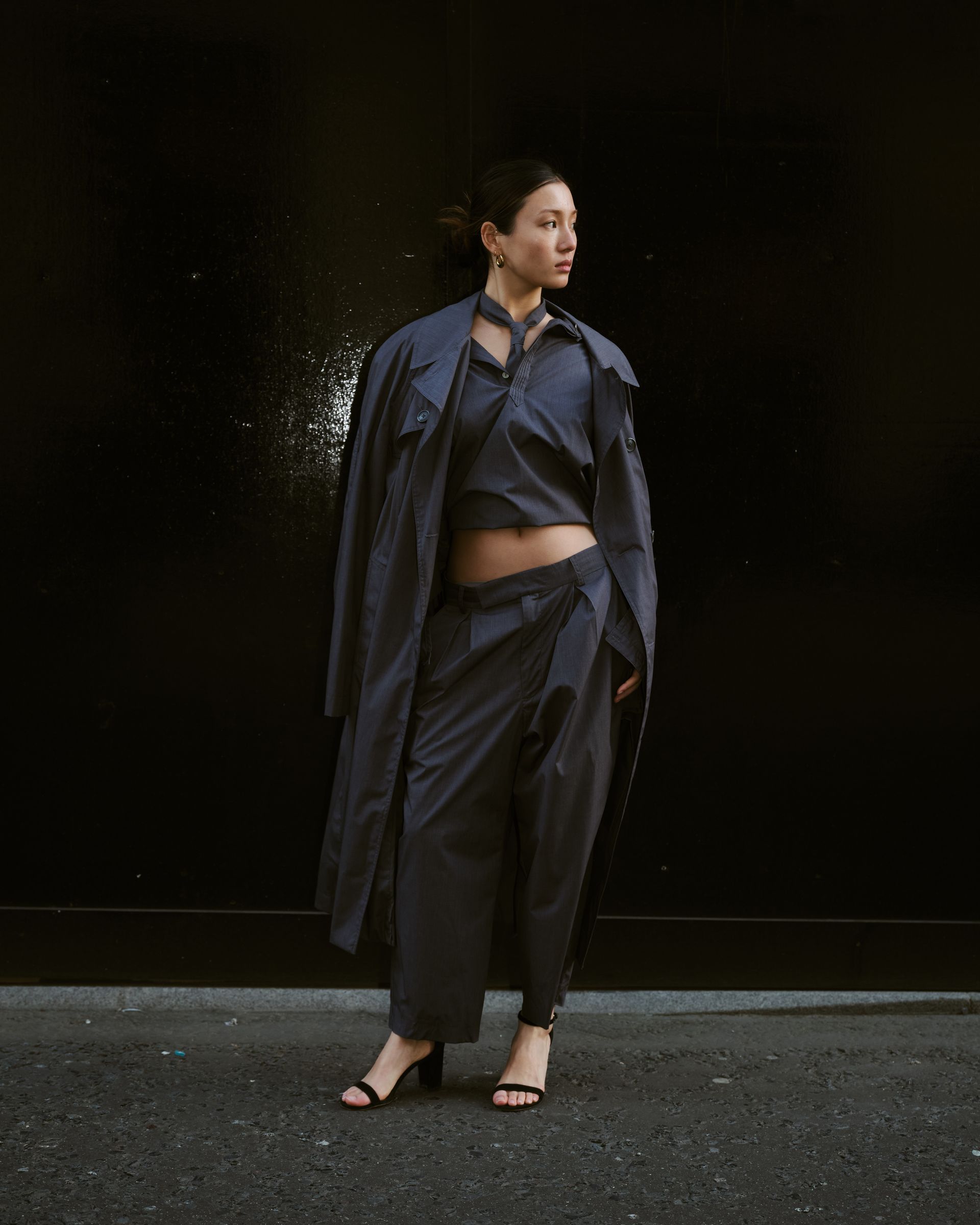 A woman is standing in front of a black wall wearing a crop top and pants.